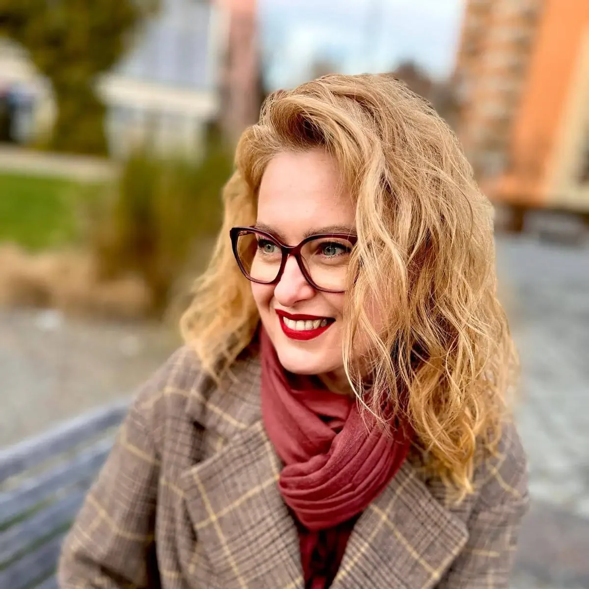 A woman in glasses and a coat stands confidently